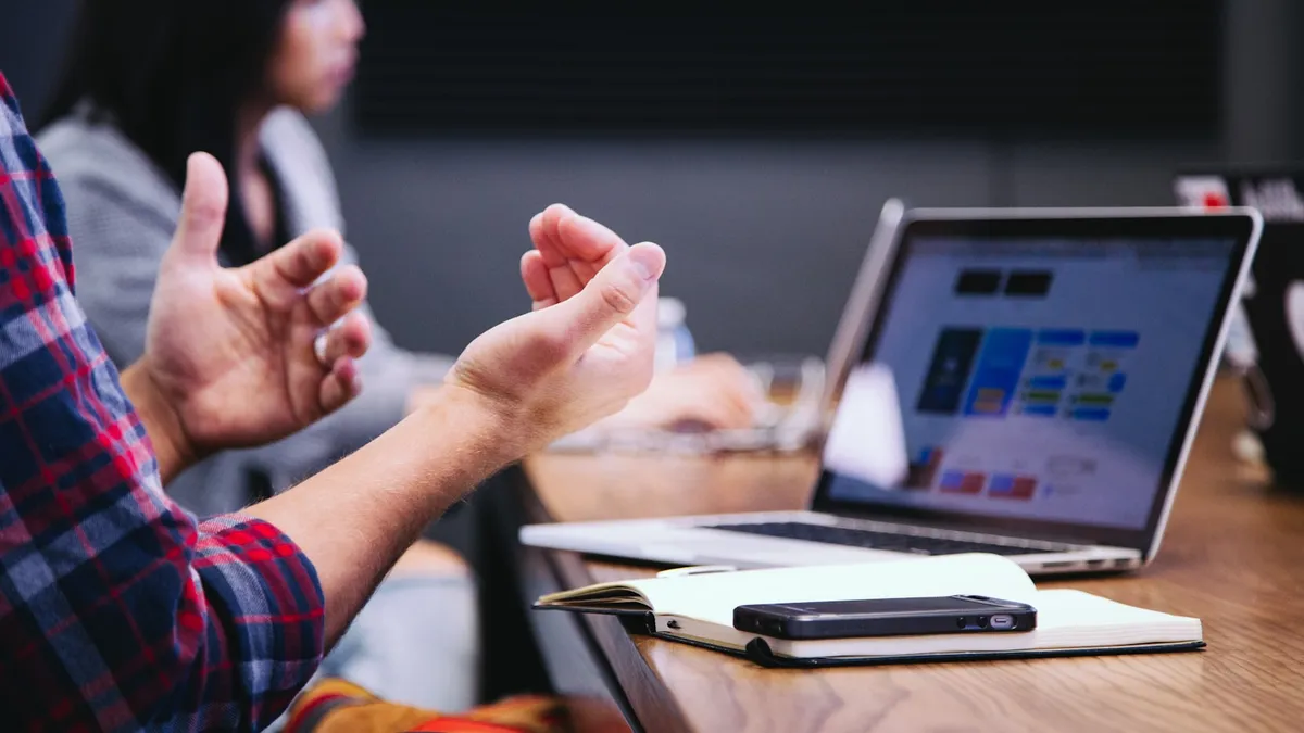 Participants gesturing in discussion at a table with laptops and notebooks