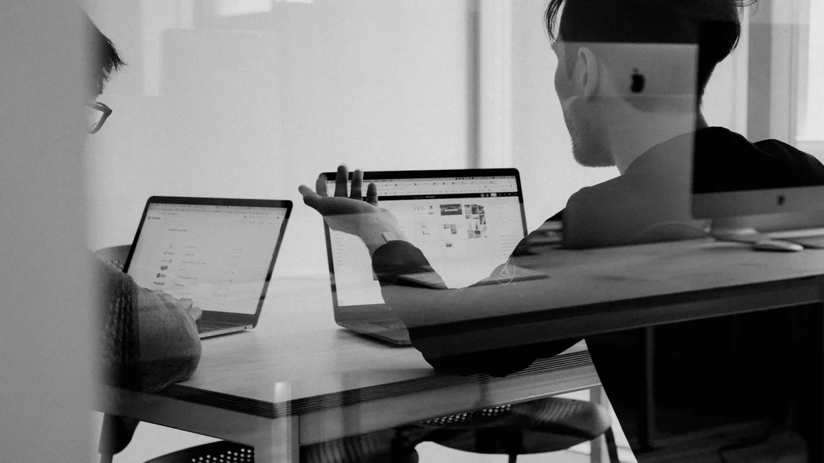 Two colleagues talking over open laptops at a shared desk
