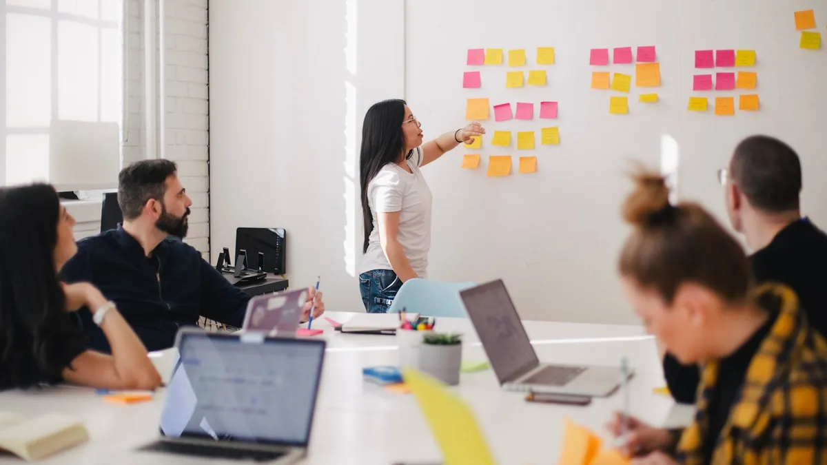 Woman mapping ideas with sticky notes on a wall as the team looks on