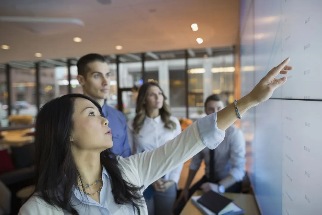 Businesswoman pointing to figures on a large display as colleagues look on