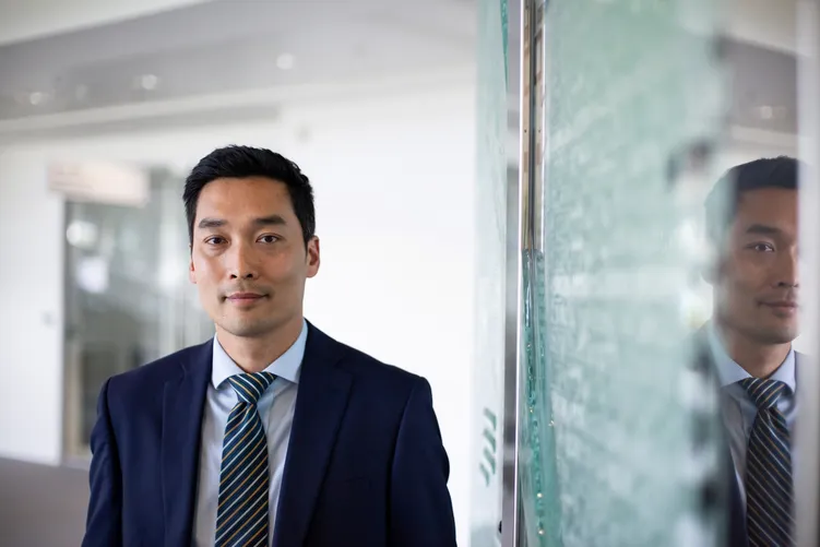 Businessman in a navy suit facing the camera beside a glass wall