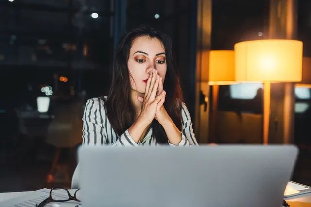 Woman studying a laptop screen intently by lamplight
