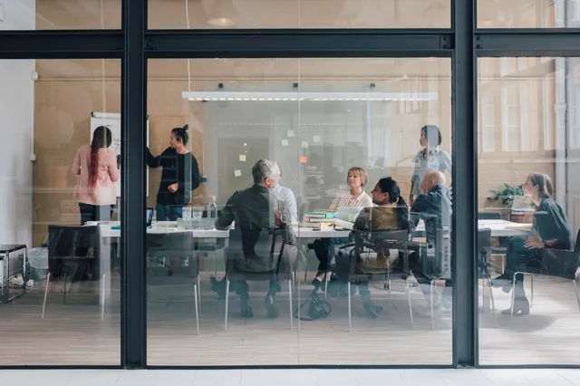 Team meeting in a glass-walled conference room with a flipchart