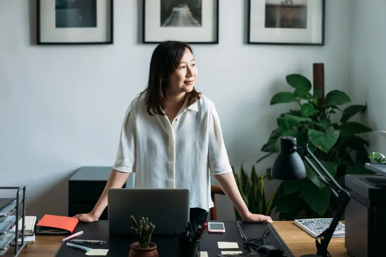 Businesswoman standing at her desk, looking out thoughtfully